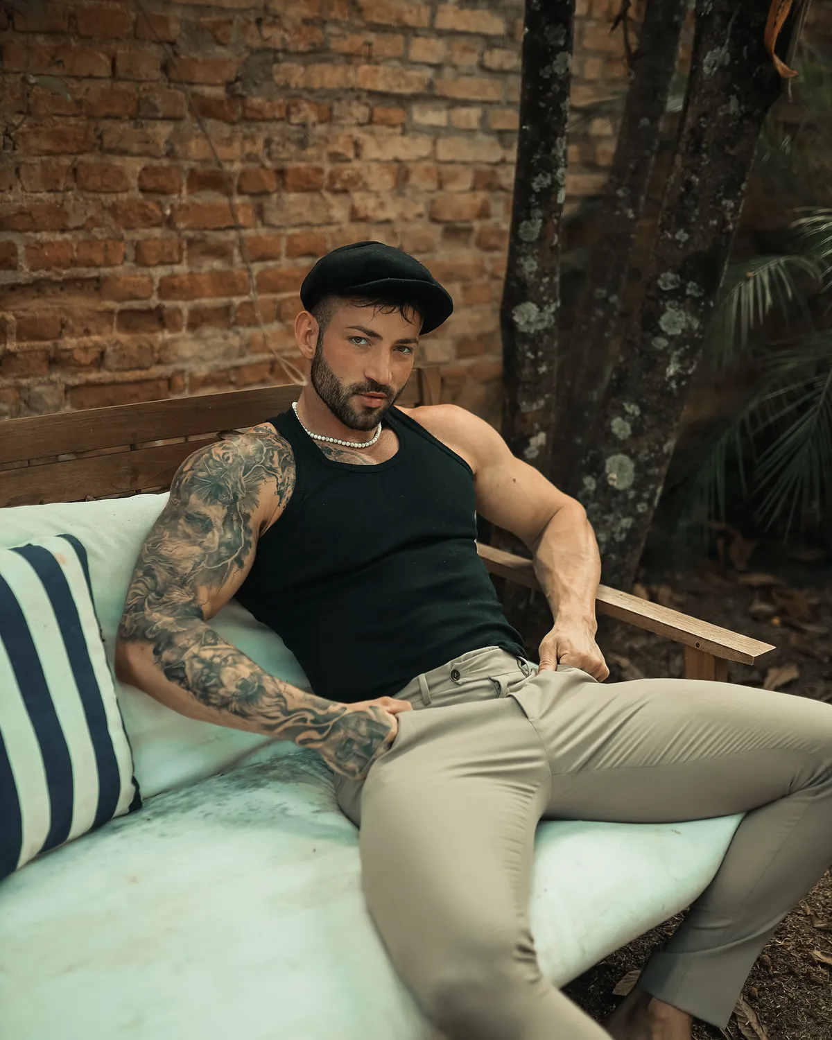 Maximo Garcia in a black tank top, sitting relaxed on a sofa outdoors